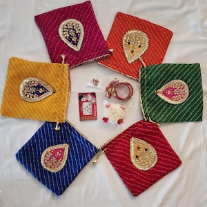 May include: An assortment of colorful, square fabric pouches with decorative gold trim and ornate, teardrop-shaped embellishments. Additional accessories include jewelry, a small garland, and a package of bindi stickers. The pouches are in various colors, including pink, orange, yellow, blue, red, and green.