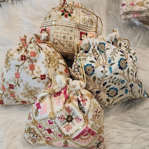 May include: Four intricately embroidered drawstring bags. The bags feature white fabric with gold, pink, and blue floral and geometric patterns. Each bag has a drawstring closure and is embellished with sequins and beads.