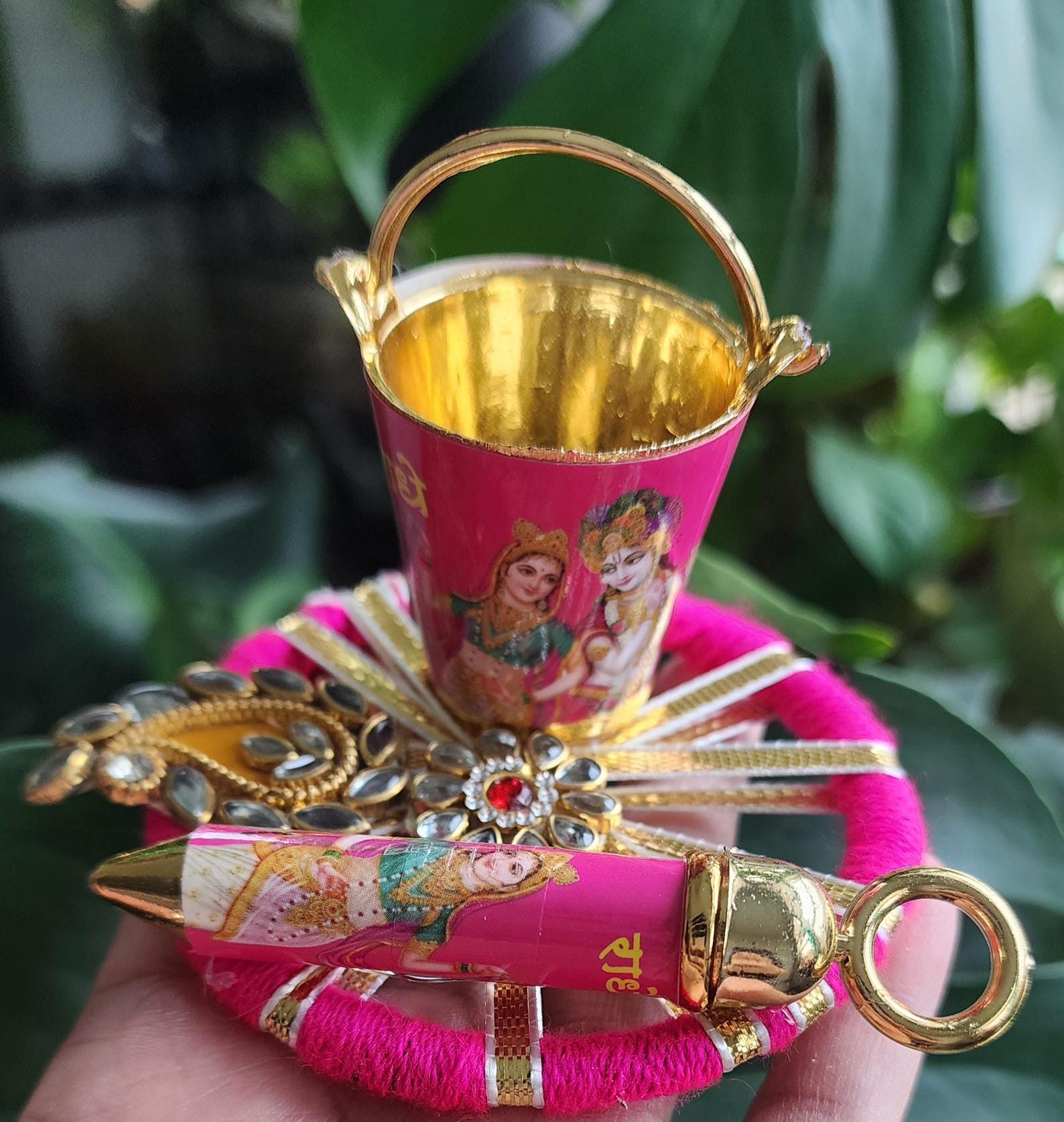 A hand holding a pink and gold pichkari set