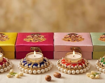 May include: Four square fabric-covered boxes in yellow, magenta, pink, and light green, each topped with a printed deity illustration. In front of each box sits a round tea light candle holder decorated with colorful thread and white pearls.