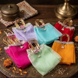 May include: A collection of six small gift bags made of sheer, colorful fabric in lavender, turquoise, red, magenta, light green, and orange. Each bag features gold metallic handles, a silver decorative trim, and a pink lotus flower charm.