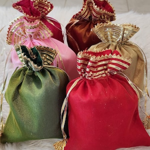 May include: Five small drawstring bags made of silk fabric with gold and red trim. The bags are in various colors, including pink, green, red, and brown.