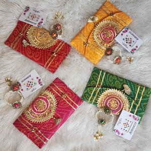 May include: Four colorful envelopes with intricate gold embroidery and embellishments. Each envelope is decorated with a different pattern and includes a small packet of decorative bindi stickers.