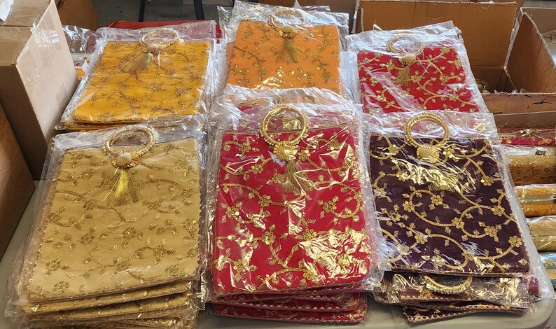 Puede incluir: Una colecci&oacute;n de peque&ntilde;as bolsas decorativas con bordados dorados y borlas. Las bolsas est&aacute;n hechas de una tela suave y texturizada y tienen un asa de anillo. Las bolsas est&aacute;n dispuestas en filas sobre una mesa.