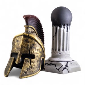 May include: A gold and black Spartan helmet with a red and brown plume sits next to a white, cracked, stone column.