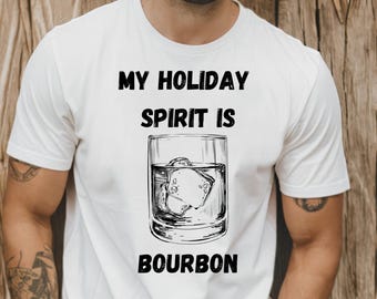 Könnte beinhalten: Weißes T-Shirt mit dem schwarzen Text "MY HOLIDAY SPIRIT IS BOURBON". Die Grafik zeigt eine detaillierte Illustration eines Bourbon-Glases mit Eis. Das Shirt ist ein Freizeitartikel.