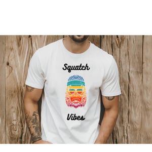 May include: White t-shirt with a rainbow colored graphic of a sasquatch wearing sunglasses and a headband. The text "Squatch Vibes" is printed below the graphic.