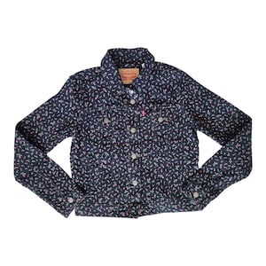 Peut inclure: Veste en jean bleu foncé avec un motif floral rose et vert. La veste a une fermeture boutonnée, deux poches poitrine et un col classique. L'étiquette de la marque Levi's est visible.