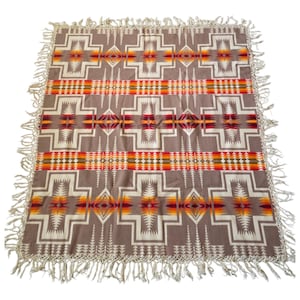 May include: A brown woven blanket with a geometric pattern in shades of red, orange, and white. The blanket has a fringe border.