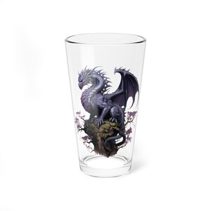 Puede incluir: Un vaso de pinta de vidrio transparente con un dragón morado posado en una rama de árbol. El dragón tiene cuernos blancos y un ala negra.