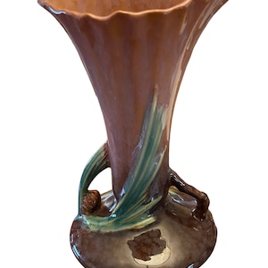 Peut inclure: Un vase en céramique brun et vert avec un motif de pomme de pin. Le vase a une ouverture large et évasée et une base étroite.