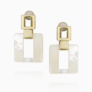Puede incluir: Un par de pendientes cuadrados dorados y blancos con un diseño geométrico. Los pendientes tienen un acabado de nácar.