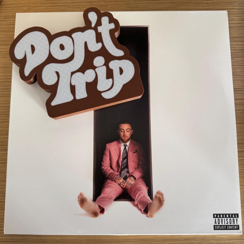 Pode incluir: Um &aacute;lbum de vinil com um &iacute;m&atilde; castanho e branco "Don't Trip" em cima. A capa do &aacute;lbum apresenta um homem de fato rosa. O &aacute;lbum tem um aviso para os pais.