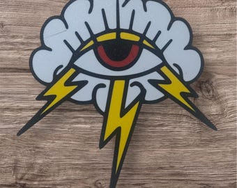 Könnte beinhalten: Ein Aufkleber mit einem stilisierten Auge in einer Wolke, mit gelben Blitzen. Das Auge hat eine rote Iris und eine gelbe Pupille. Die Wolke ist hellgrau mit schwarzen Umrissen, und die Blitze sind gelb mit schwarzen Umrissen.