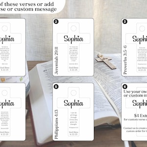 May include: White cross-shaped cards with the name "Sophia" and Bible verses printed on them. The cards are displayed on a wooden surface next to an open book and a small wooden cross. The text "Choose one of these verses or add your own verse or custom message" is at the top.