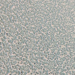 May include: Close-up of a textured surface with a pattern of small, irregular bumps. The surface has a light blue-green color with a slightly off-white background, creating a mottled appearance. The texture is rough and uneven.