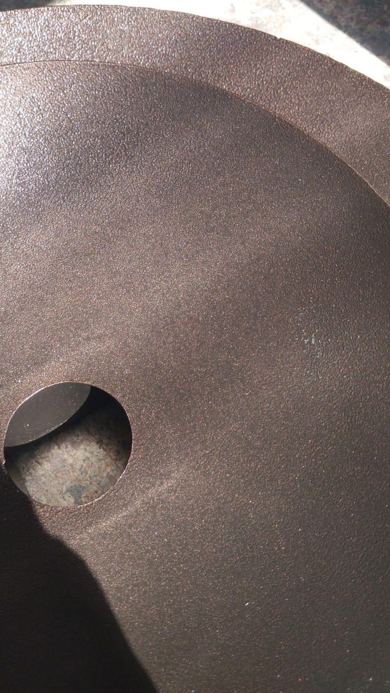 May include: Close-up of a dark brown, textured metal surface with a circular hole. The surface has a slightly rough, speckled appearance, and the hole is smooth and dark.