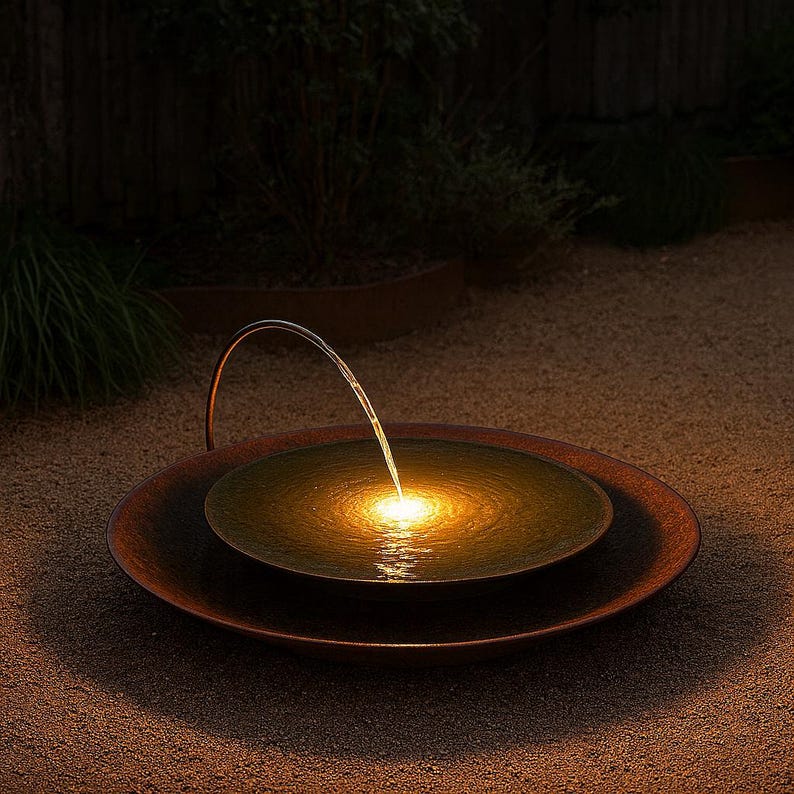 May include: Outdoor water fountain with a copper-colored basin. A curved metal spout arches over the water, creating a gentle stream. The water is illuminated by a warm, golden light, creating a tranquil ambiance in the garden.