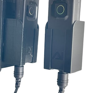 May include: Two black battery packs with cords and a black connector. The battery packs have a small green light on the front.