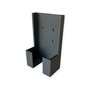 Op de afbeelding: Zwarte plastic wandbeugel met een gleuf om een telefoon of ander apparaat vast te houden. De beugel heeft vier gaten om hem aan een muur te bevestigen.