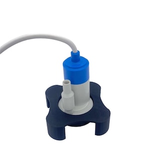 Puede incluir: Una pequeña bomba de agua sumergible blanca y azul con una base negra. La bomba tiene un cable blanco y una parte superior azul.