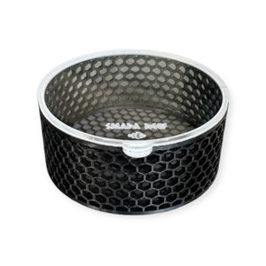 May include: A black, cylindrical container with a honeycomb pattern and a silver rim. The text "SMADA BEEF" is printed on the inside base. The container has a small, white handle-like protrusion.