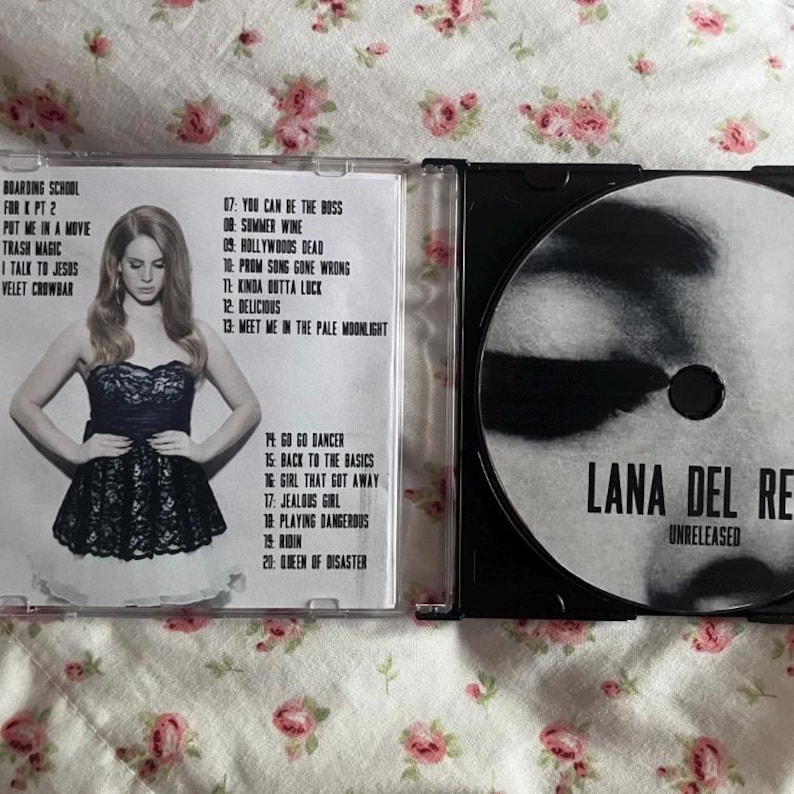 May include: A CD case with a photo of a woman in a black dress. The CD case is open, revealing the CD and tracklist. The CD is labeled "Lana Del Rey Unreleased."