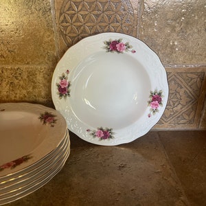 May include: A set of white porcelain soup bowls with a gold rim and a floral design featuring pink roses. The bowls are stacked on top of each other.