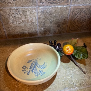 Puede incluir: Un tazón de cerámica marrón claro con un diseño floral azul y blanco. El tazón está sobre una superficie de azulejos.