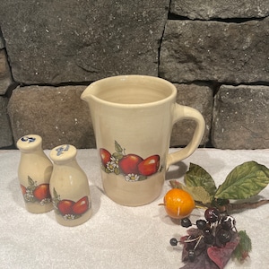 May include: A set of three ceramic kitchenware items with an apple and flower design. The set includes a pitcher and two salt and pepper shakers.
