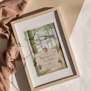May include: A framed invitation for "Harper's First Birthday" with an "Alice in Wonderland" theme. The illustration features forest scenery and characters from the story. The frame is light wood.