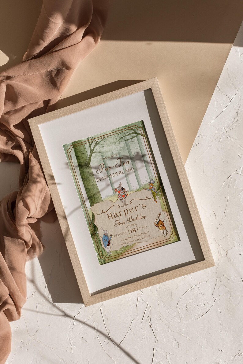 May include: A framed invitation for "Harper's First Birthday" with an "Alice in Wonderland" theme. The illustration features forest scenery and characters from the story. The frame is light wood.