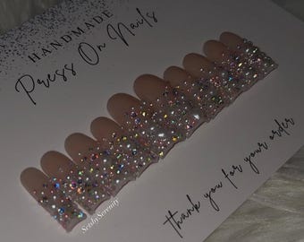 May include: Handmade press-on nails with a nude base and a sparkling, glittery design along the tips. The nails are arranged on a card with the text "Handmade Press On Nails" and "thank you for your order". The design includes iridescent rhinestones and pearls.