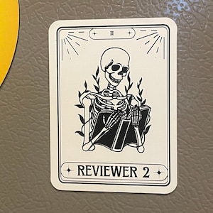 May include: A white card with black text and a black and white illustration of a skeleton sitting and reading a book. The card has the text "REVIEWER 2" and the Roman numeral "II" at the top.