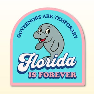 May include: A sticker with a cartoon manatee illustration. The manatee is gray with a smiling face and raised arm. The sticker has the text "Governors Are Temporary" and "Florida Is Forever". The background is light blue with a pink border.