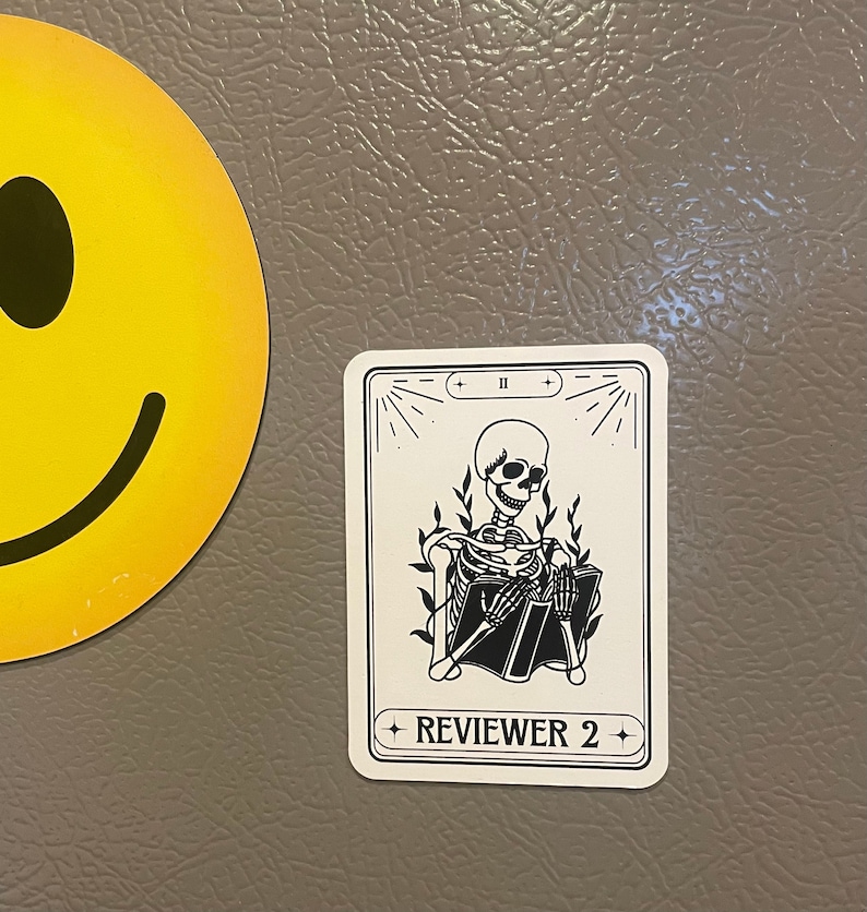 May include: A white card with black text and a black and white illustration of a skeleton sitting and reading a book. The card has the text "REVIEWER 2" and the Roman numeral "II" at the top.