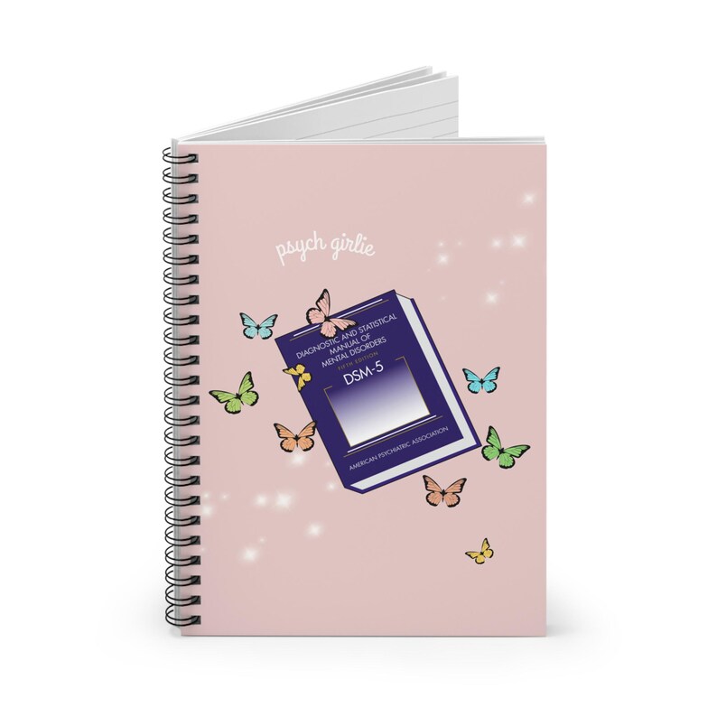 Puede incluir: Cuaderno de espiral rosa con la inscripci&oacute;n "psych girlie" y un gr&aacute;fico del libro DSM-5. La portada est&aacute; decorada con mariposas de colores y brillos. El cuaderno est&aacute; dise&ntilde;ado para los entusiastas de la salud mental.