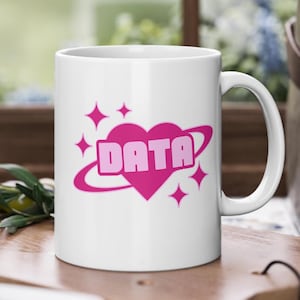 May include: White ceramic mug with a pink heart design featuring the word "DATA" inside the heart. The heart is surrounded by a pink ring and pink stars.