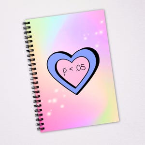 May include: Spiral-bound notebook with a pastel rainbow background. A blue and black heart shape contains a smaller pink heart with the text "p < .05". The notebook has a white background and a black spiral binding.