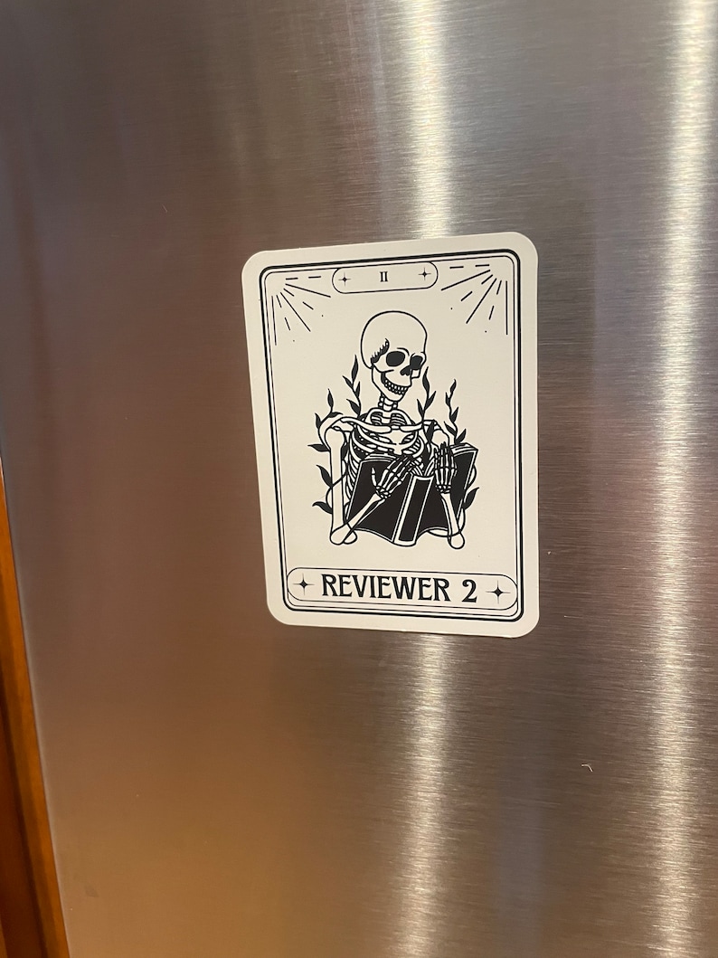 May include: A black and white illustration of a skeleton reading a book. The illustration is on a white card with black text that reads "REVIEWER 2" and "II".