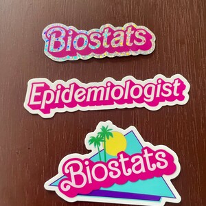 Pode incluir: Tr&ecirc;s adesivos com as palavras "Biostats" e "Epidemiologista" em letras rosa e brancas. O adesivo inferior apresenta um "Biostats" rosa e branco com um gr&aacute;fico de palmeira e sol em um tri&acirc;ngulo azul e roxo.