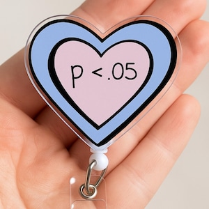 May include: A heart-shaped badge reel with a light blue and pink design. The badge reel has the text "p < .05" in black. The badge reel is attached to a retractable cord and a clear plastic clip.
