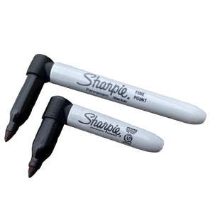 May include: Two black Sharpie permanent markers, one with a fine point and the other a mini fine point. Both markers have white barrels with black lettering.
