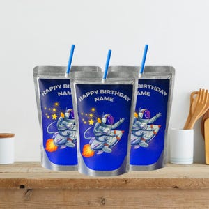 May include: Three silver pouches with blue straws. Each pouch has a blue background with an astronaut graphic and the text "HAPPY BIRTHDAY NAME". The astronaut is riding a rocket with flames and stars.