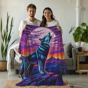 May include: A rectangular throw blanket featuring a vibrant graphic print of a wolf howling at a large moon. The design displays a mountain landscape with purple, blue, and orange sunset colors, showcasing a wolf standing on a rocky cliff edge.