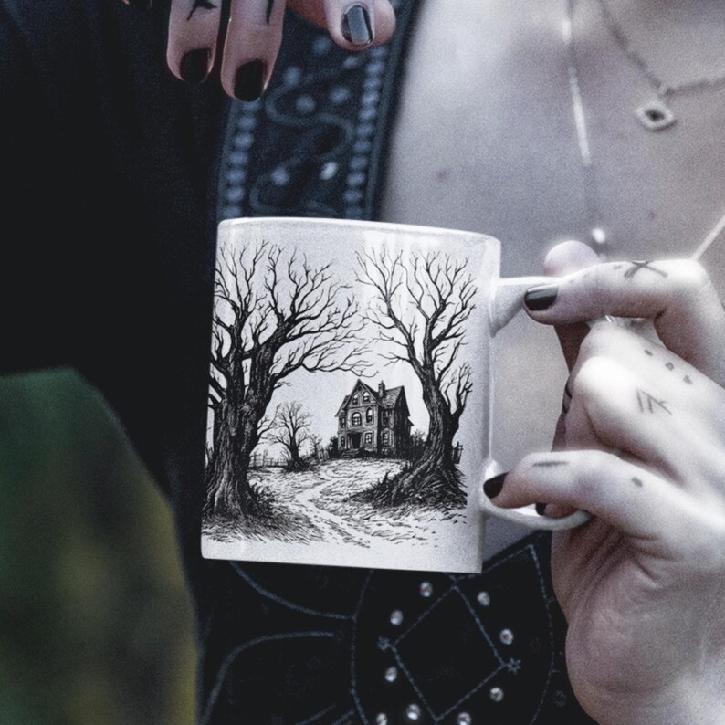 May include: White ceramic mug with a black and white illustration of a spooky house with trees on a path. The house has a pointed roof and windows.