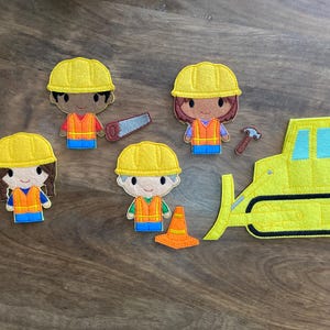 May include: A set of felt finger puppets featuring construction workers, a bulldozer, a stop sign, and a traffic cone. The puppets are yellow and orange with black outlines. The bulldozer is yellow with black wheels and a blue windshield.