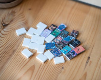 May include: A collection of miniature books with colorful covers, arranged on a wooden surface with white tiles. The books feature titles like "Blood Ritual" and "The Darkling".