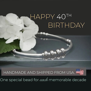 May include: A silver bracelet with four beads, representing four decades, with the text "HAPPY 40TH BIRTHDAY" and "HANDMADE AND SHIPPED FROM USA."  One special bead for each memorable decade.