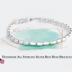 May include: A handmade sterling silver bracelet featuring rice-shaped beads. The bracelet is displayed on a white background with a watercolor design and the text "Handmade All Sterling Silver Rice Bead Bracelet".